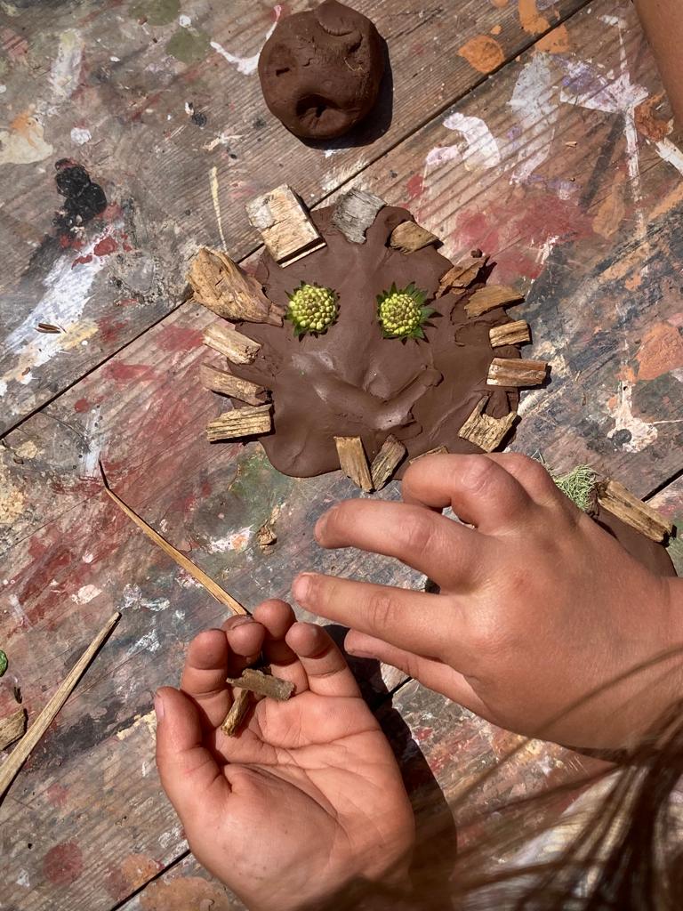 Child's hands making a clay face with natural materials.