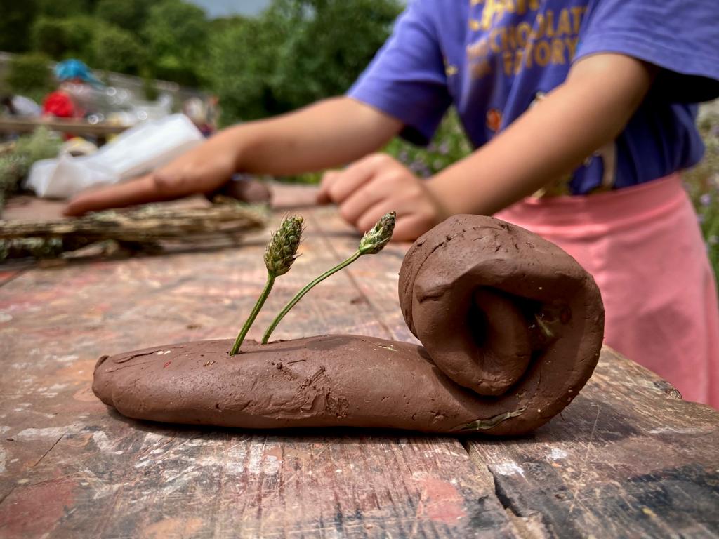 A clay snail with leaf antennae. A child making in the background.