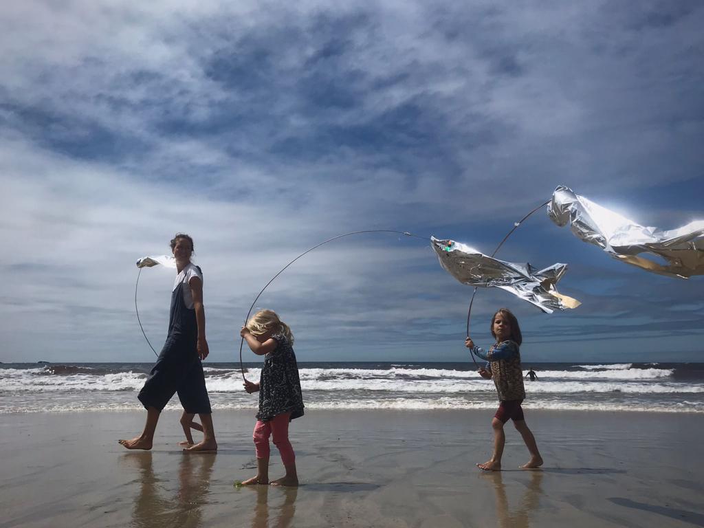 Three people fly hand-made fish kites on a beach