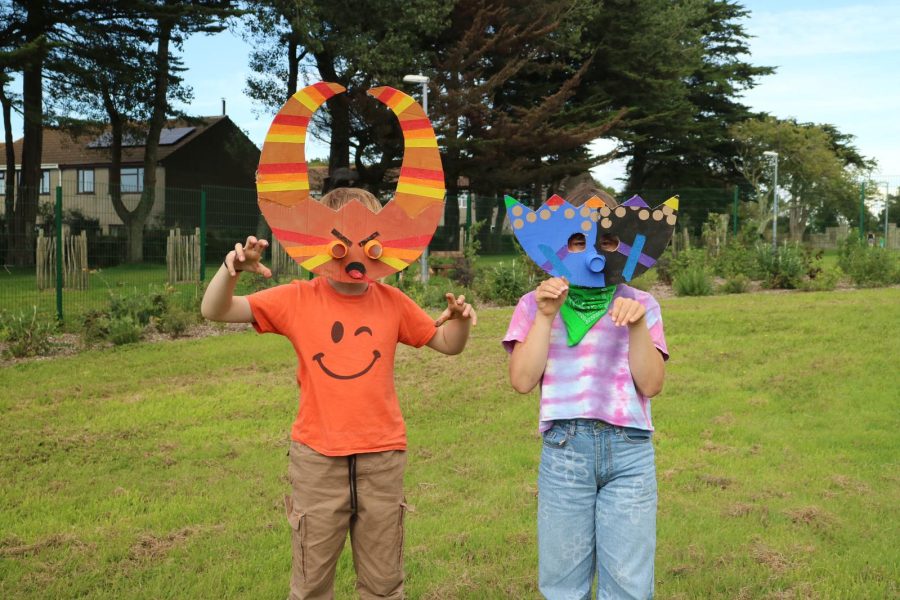 Two children wear colourful hand-made folk masks in a field