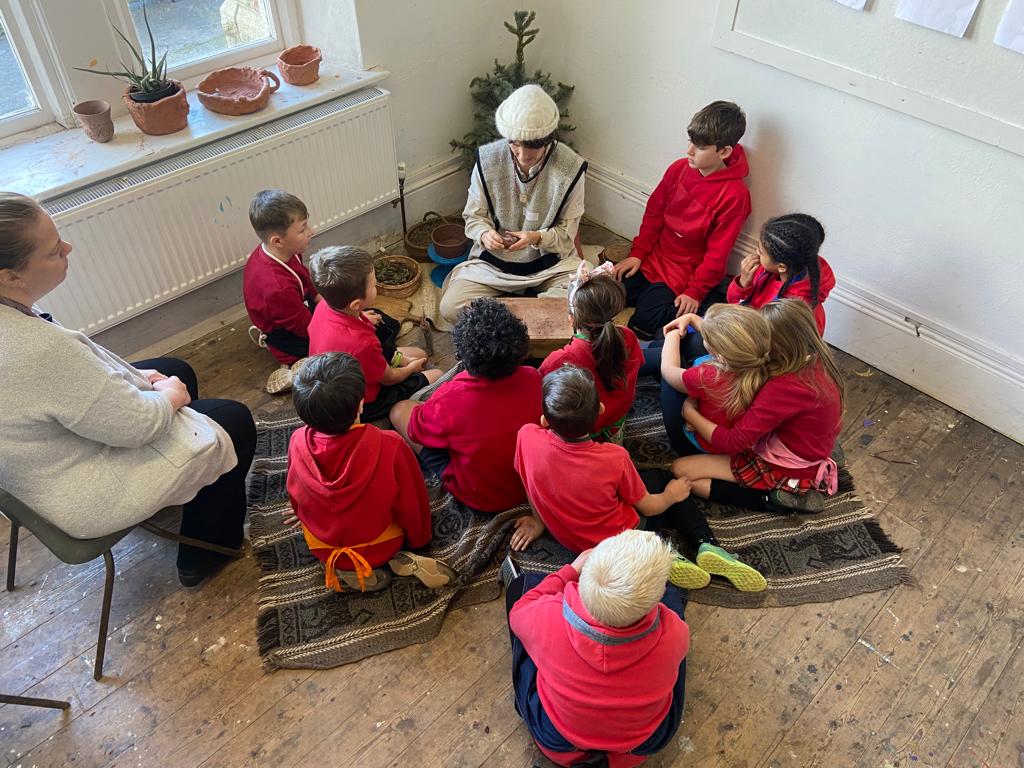 Children sit around a lady showing them pottery artefacts