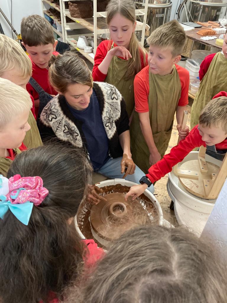 Children gather around a demonstration of throwing a clay pot on a potter's wheel