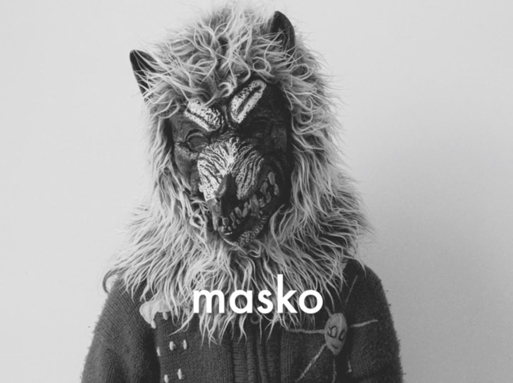 Black and white image of a child in a fluffy animal mask, with painted face, titled with the word 'masko'.