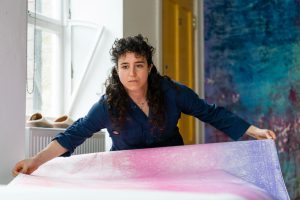 The artist stretching to position a large pink and purple print. 