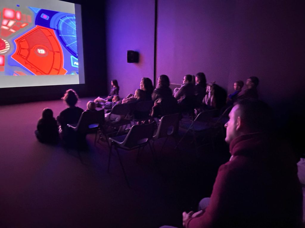 A group of people sat together watching a film in a dark room