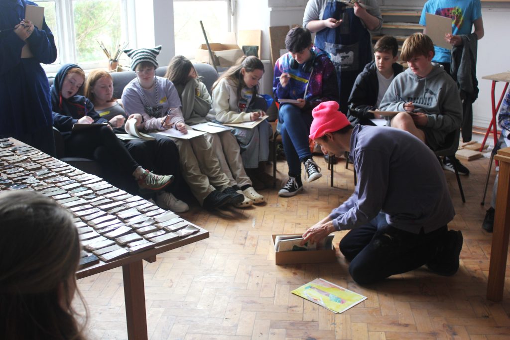 A group of young people gathered looking at an artist showing his work